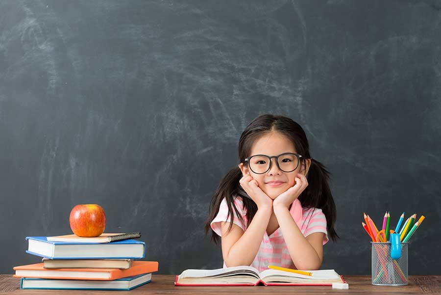 cheerful girl seating at class table with book open